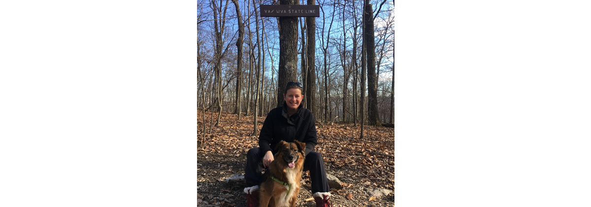 Meagan sitting against a tree in the woods with her dog.